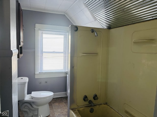 full bath featuring stone finish floor, vaulted ceiling, toilet, and shower / washtub combination