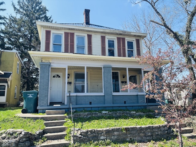 view of front facade with brick siding, covered porch, and a chimney