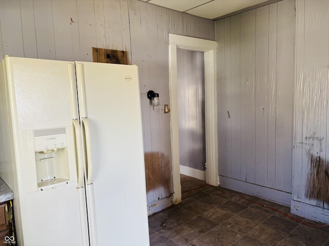 kitchen featuring wood walls and white fridge with ice dispenser