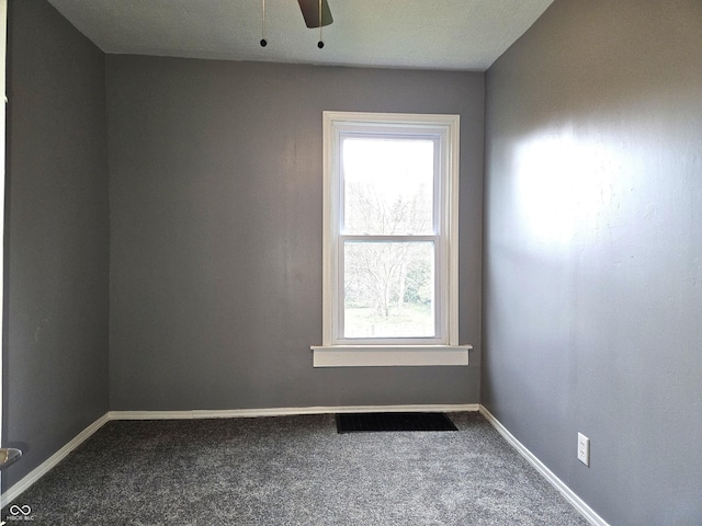 empty room featuring dark colored carpet, visible vents, baseboards, and ceiling fan