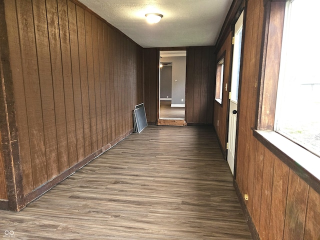 hallway with a textured ceiling, wood walls, and dark wood finished floors