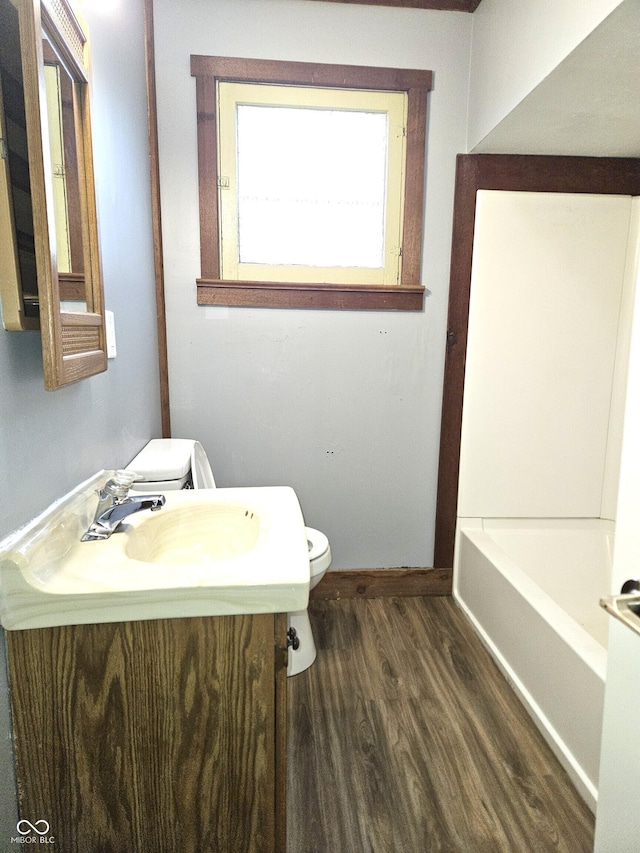 bathroom featuring vanity, baseboards, toilet, a washtub, and wood finished floors