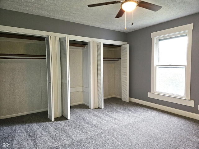 unfurnished bedroom featuring carpet, multiple windows, two closets, and a textured ceiling