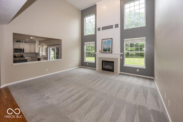 11648 Stickney Ct, Fishers, IN 46037 - unfurnished living room featuring baseboards, high vaulted ceiling, a fireplace with flush hearth, a sink, and light colored carpet