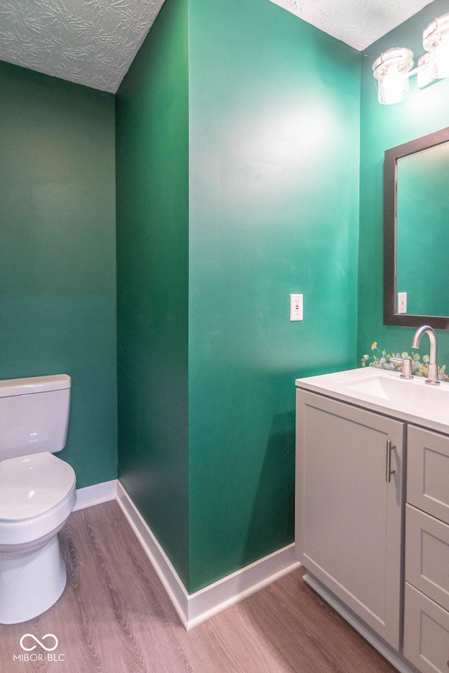 half bath featuring a textured ceiling, wood finished floors, baseboards, vanity, and toilet
