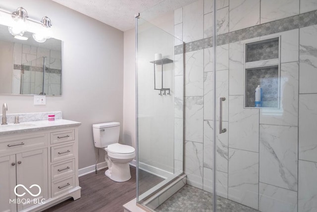 full bathroom featuring a textured ceiling, wood finished floors, vanity, toilet, and a marble finish shower