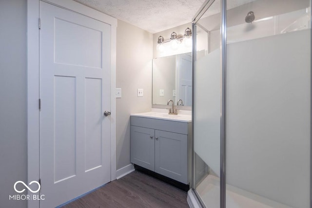 full bathroom with a textured ceiling, vanity, a stall shower, and wood finished floors