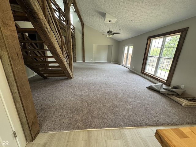 unfurnished living room with lofted ceiling, baseboards, ceiling fan, a textured ceiling, and carpet flooring