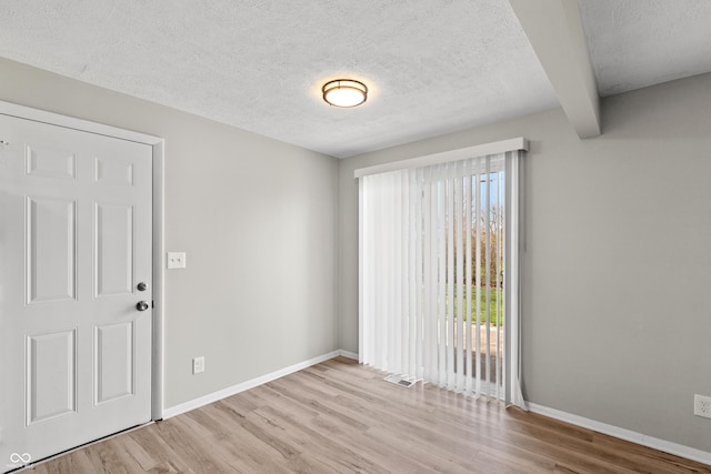 spare room featuring wood finished floors, a textured ceiling, baseboards, and visible vents
