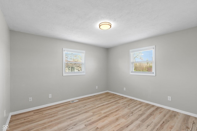 unfurnished room with light wood-type flooring, visible vents, and a wealth of natural light