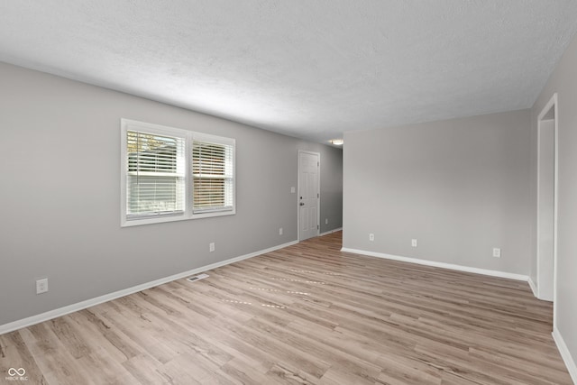 empty room with baseboards, a textured ceiling, and light wood-style floors