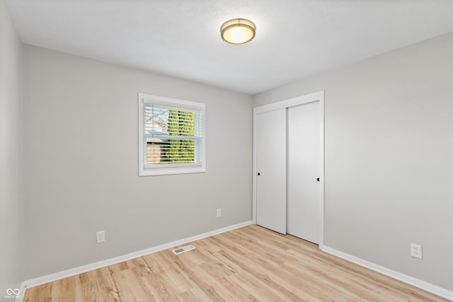 unfurnished bedroom featuring light wood-type flooring, baseboards, visible vents, and a closet