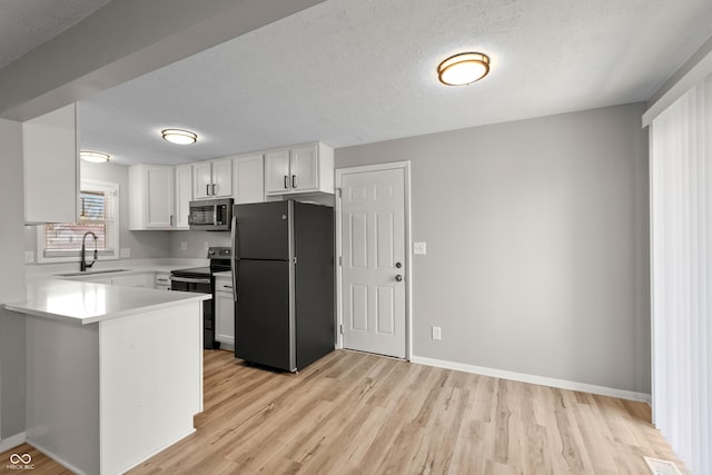 kitchen featuring light wood-style flooring, a sink, white cabinetry, light countertops, and appliances with stainless steel finishes