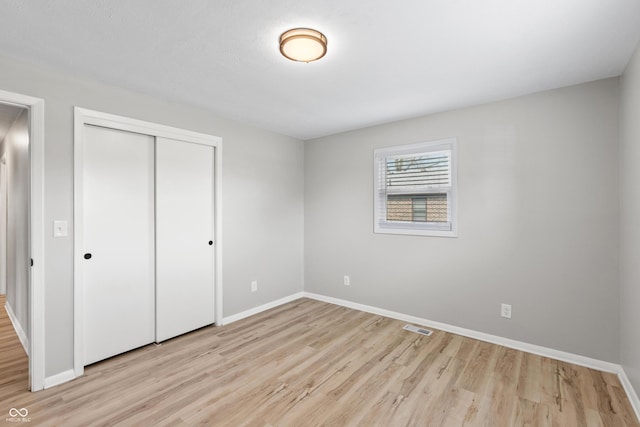 unfurnished bedroom with light wood finished floors, baseboards, visible vents, and a closet