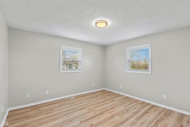 unfurnished room featuring wood finished floors, a wealth of natural light, baseboards, and visible vents