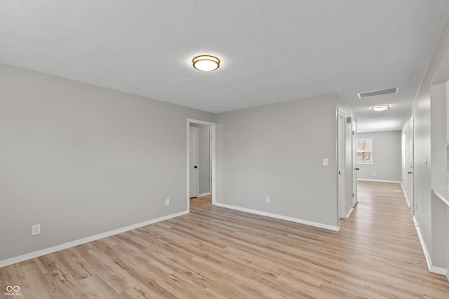 empty room featuring light wood-type flooring, visible vents, and baseboards