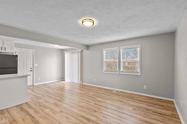 unfurnished living room with baseboards, visible vents, a textured ceiling, and light wood finished floors