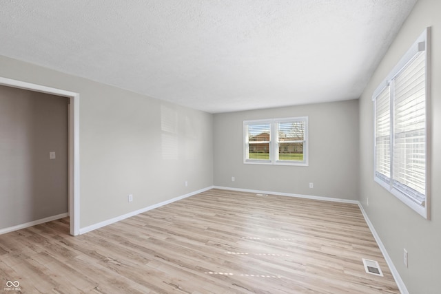 empty room featuring a textured ceiling, light wood-style flooring, visible vents, and baseboards