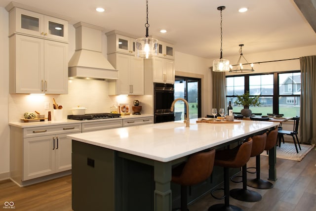 kitchen featuring an island with sink, dark wood-type flooring, gas stovetop, custom range hood, and a sink