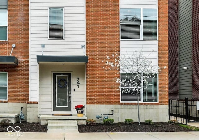 doorway to property featuring brick siding and fence