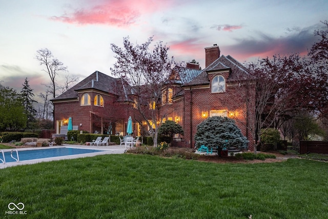 290 Breakwater Dr, Fishers, IN 46037 - back of property at dusk with a chimney, brick siding, a yard, an outdoor pool, and a patio area