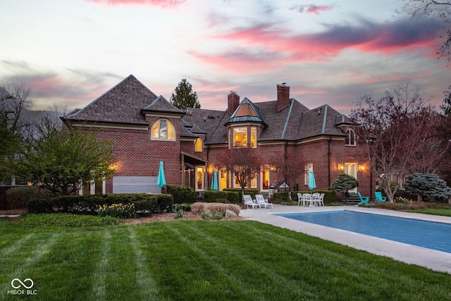 290 Breakwater Dr, Fishers, IN 46037 - back of property at dusk with brick siding, a yard, a chimney, and an outdoor pool