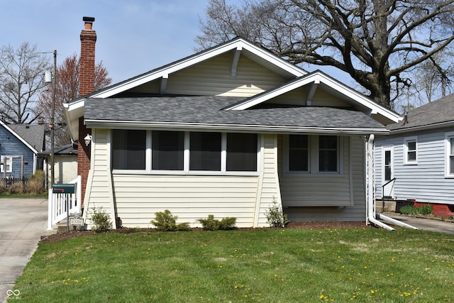 bungalow featuring a front lawn, a chimney, and a shingled roof