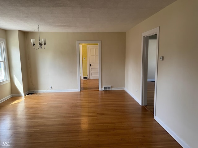 unfurnished room with an inviting chandelier, a textured ceiling, visible vents, wood finished floors, and baseboards