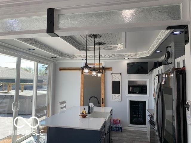 kitchen featuring a raised ceiling, a sink, light countertops, an island with sink, and black appliances