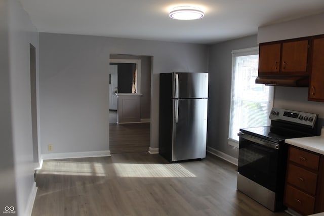 kitchen with appliances with stainless steel finishes, light countertops, baseboards, under cabinet range hood, and dark wood-type flooring