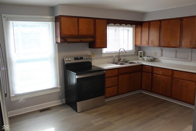 kitchen with a sink, stainless steel range with electric stovetop, light countertops, under cabinet range hood, and visible vents