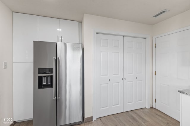 kitchen with white cabinets, light stone countertops, stainless steel fridge with ice dispenser, light wood-type flooring, and visible vents