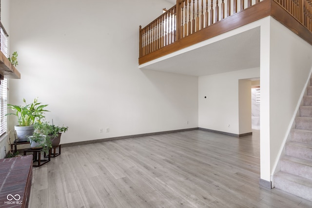 unfurnished living room featuring baseboards, stairs, wood finished floors, and a wealth of natural light