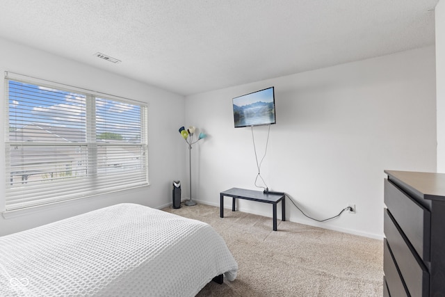 bedroom featuring a textured ceiling, baseboards, visible vents, and light carpet