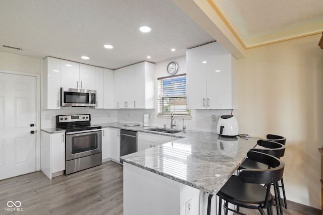 kitchen with visible vents, a peninsula, a kitchen bar, a sink, and appliances with stainless steel finishes
