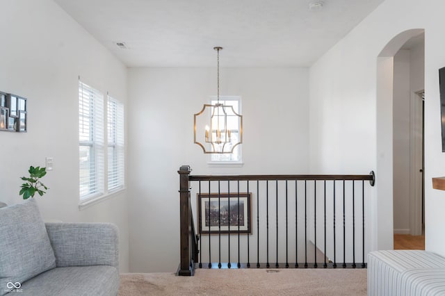 interior space with an inviting chandelier, visible vents, arched walkways, carpet flooring, and an upstairs landing