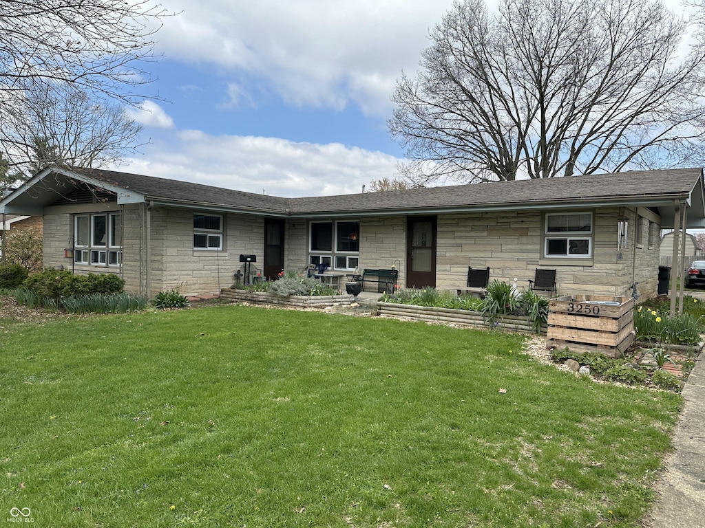 back of property with stone siding, a lawn, and roof with shingles