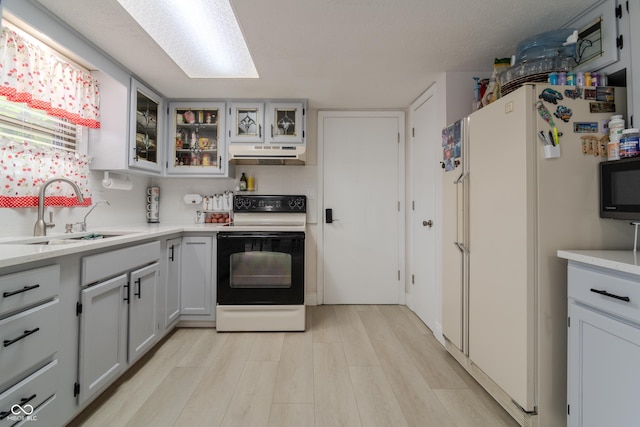kitchen featuring a sink, light countertops, electric range, under cabinet range hood, and freestanding refrigerator