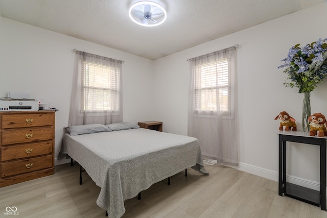 bedroom with baseboards, multiple windows, and light wood-style flooring