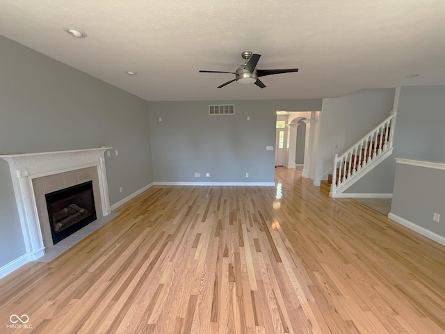 3724 Jonathan Rdg, Columbus, IN 47201 - unfurnished living room featuring a ceiling fan, a tiled fireplace, light wood-style flooring, stairs, and arched walkways