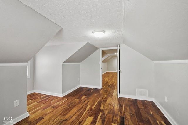 bonus room with a textured ceiling, baseboards, wood finished floors, lofted ceiling, and visible vents