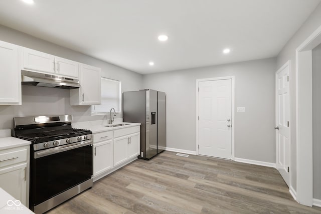 kitchen featuring appliances with stainless steel finishes, a sink, white cabinets, light wood-style floors, and under cabinet range hood