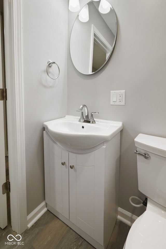 half bath with baseboards, wood finished floors, toilet, and vanity