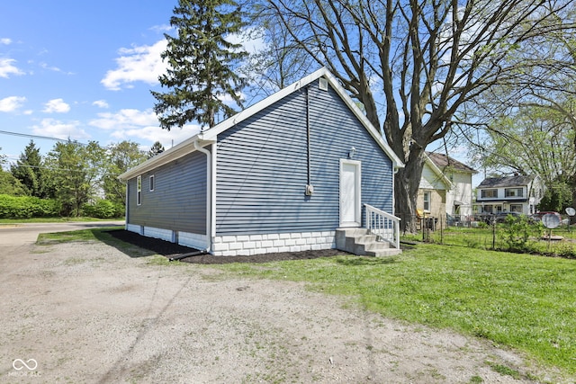 view of property exterior with entry steps, fence, and a lawn