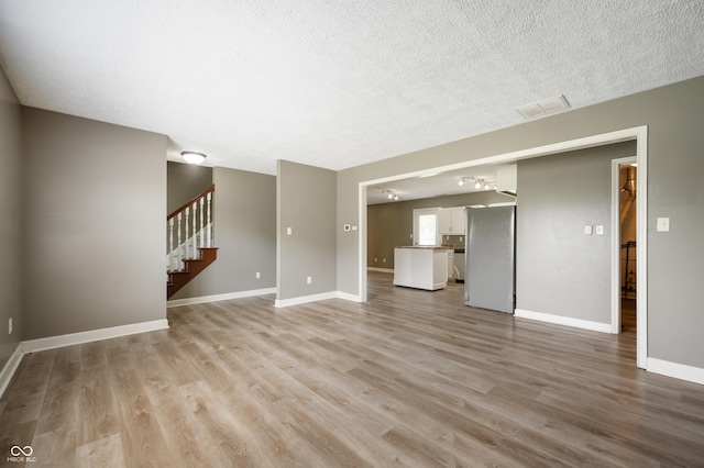 4786 N Mill Ct, Greenfield, IN 46140 - unfurnished living room with light wood-style flooring, stairway, baseboards, and a textured ceiling