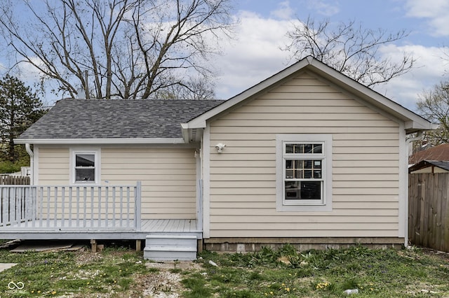 view of home's exterior featuring fence, a wooden deck, and a shingled roof