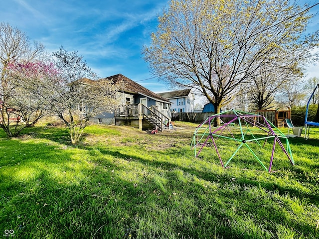 view of yard with a trampoline, a playground, fence, a wooden deck, and stairs