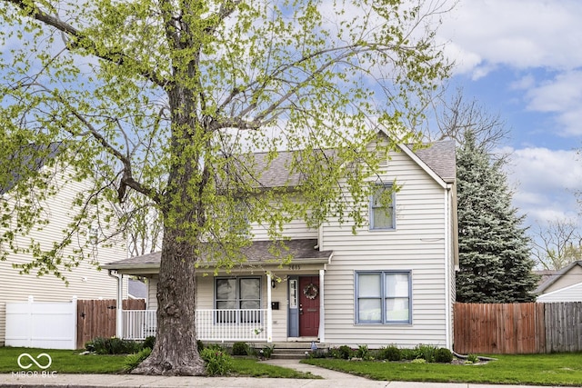 traditional-style house featuring a porch, a front lawn, fence, and roof with shingles