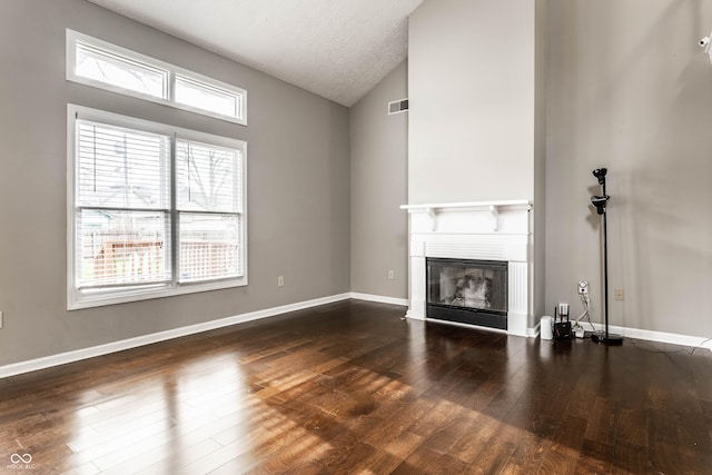 unfurnished living room with hardwood / wood-style floors, vaulted ceiling, visible vents, baseboards, and a glass covered fireplace