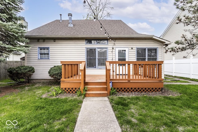 rear view of property with a lawn, a shingled roof, and fence